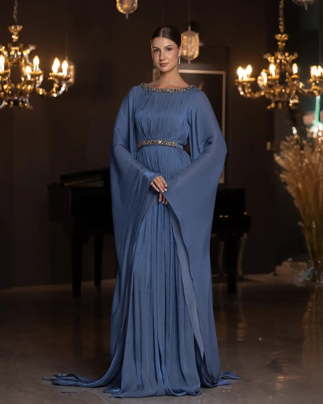 Bloom Dress - Elegant Blue Chiffon with pleated skirt and cape sleeves, styled for formal evening wear under chandelier lighting.