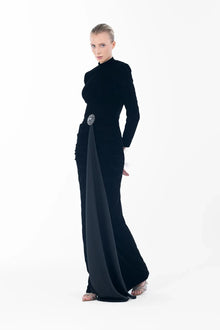 Elegant Noir Velvet Gown from Artista Eid - AW 2025 with a jeweled brooch and side drape, ideal for formal evening wear.