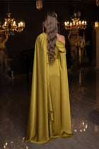 Back view of Verite Majestique PF2025 Ambre Dress in olive green satin, showcasing long draped cape and elegant one-shoulder silhouette.