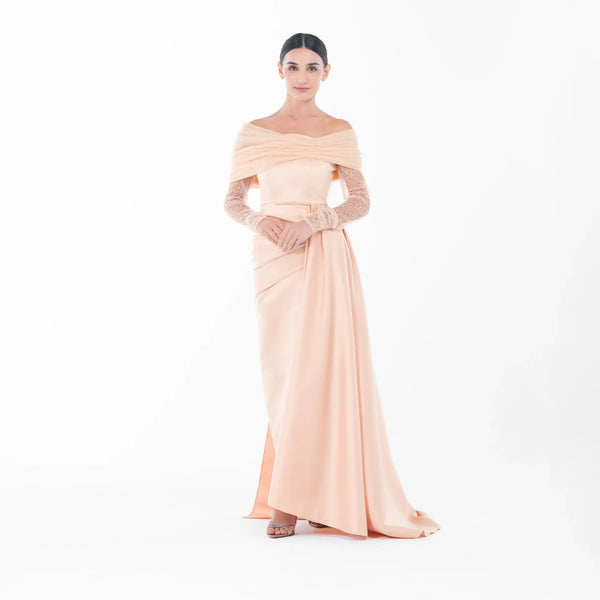 Model wearing the Ispahan Dress, an apricot off-shoulder gown with lace sleeves, showcasing luxury evening wear style.