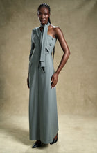 Woman wearing a long, light gray dress with buttons against a beige background