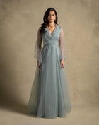 Elegant woman in a sage green Gilded Dress featuring sheer sleeves and a flowing skirt, perfect for evening wear and high-end fashion.