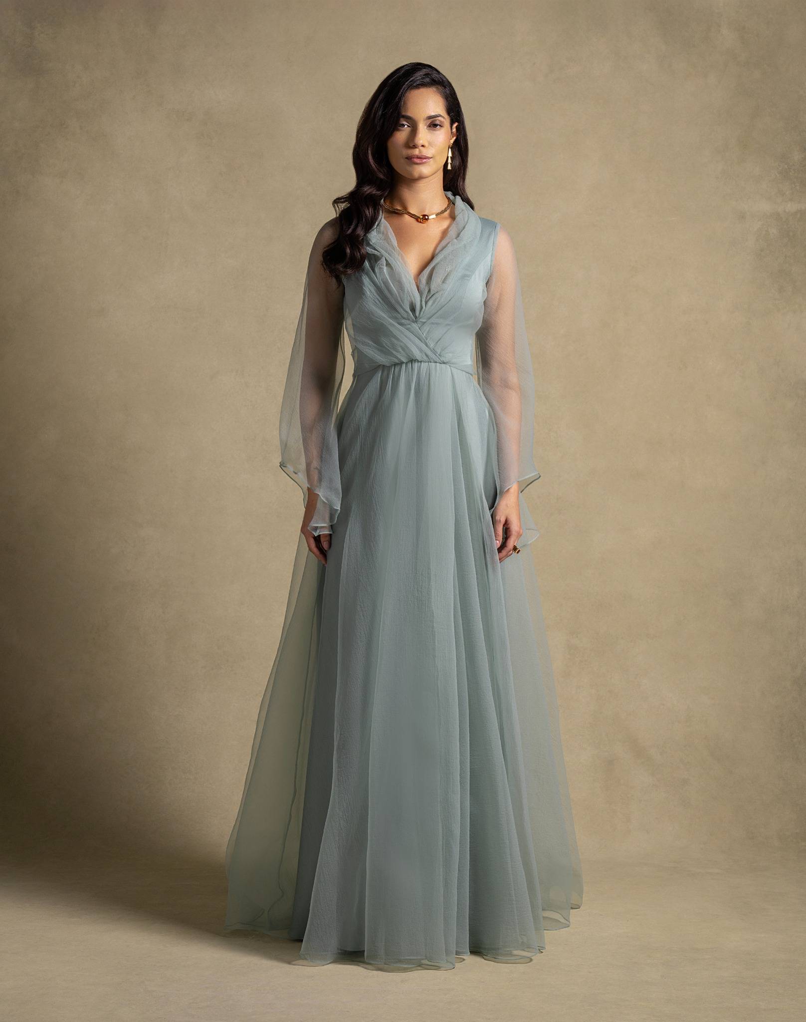 Elegant woman in a sage green Gilded Dress featuring sheer sleeves and a flowing skirt, perfect for evening wear and high-end fashion.