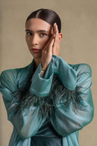 Elegant model showcasing the Blanche Set from the Zarina Collection in emerald green satin with feather-trimmed cuffs.