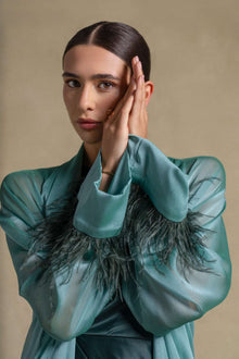 Elegant model showcasing the Blanche Set from the Zarina Collection in emerald green satin with feather-trimmed cuffs.