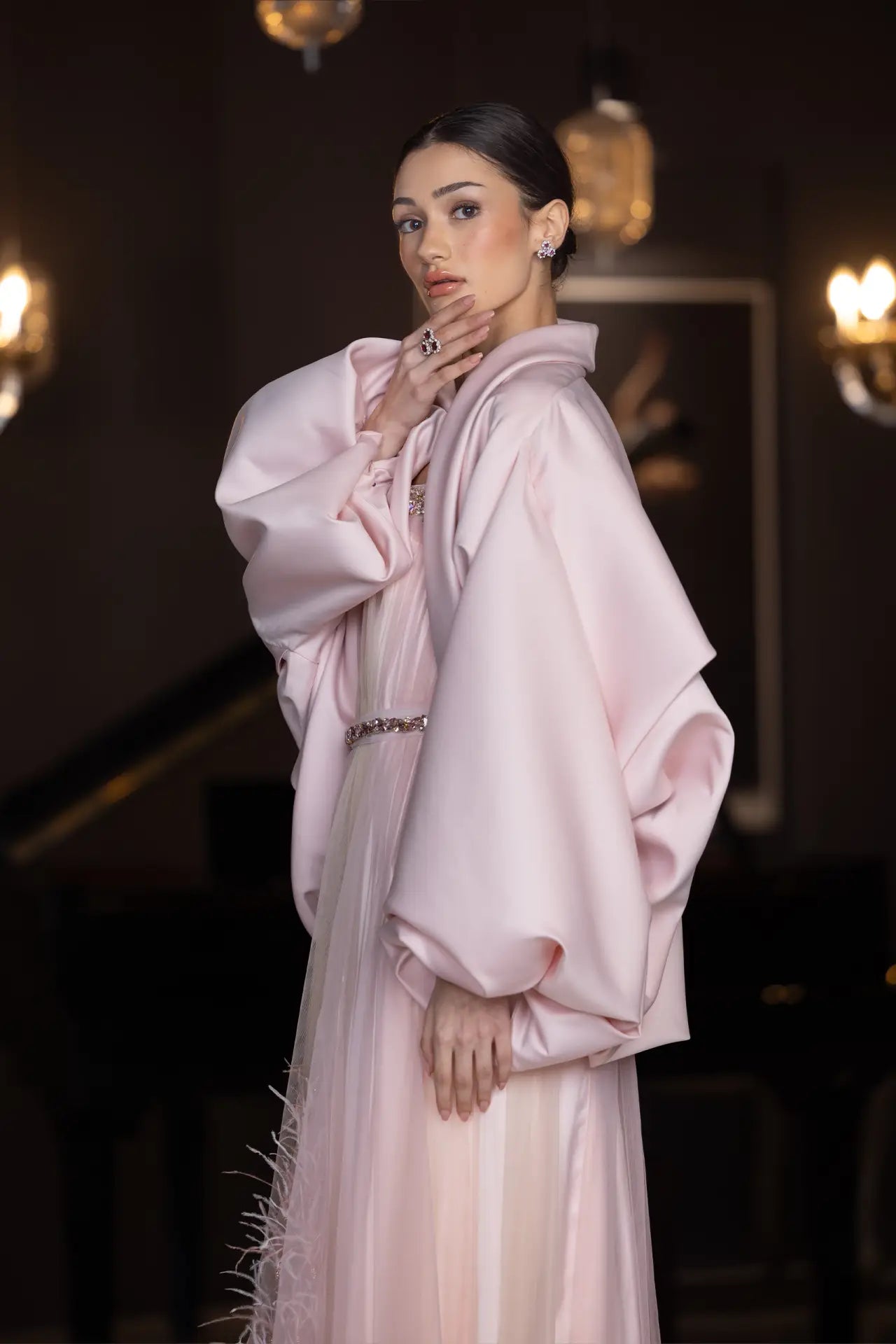 Model in Miss Waad Dress - Vérité Majestique PF2025 wearing voluminous blush cape and soft pink gown with feathered detailing.