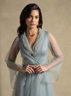 Model wearing Gilded Dress from the Zarina Collection, showcasing its elegant sage green fabric and sheer organza sleeves.