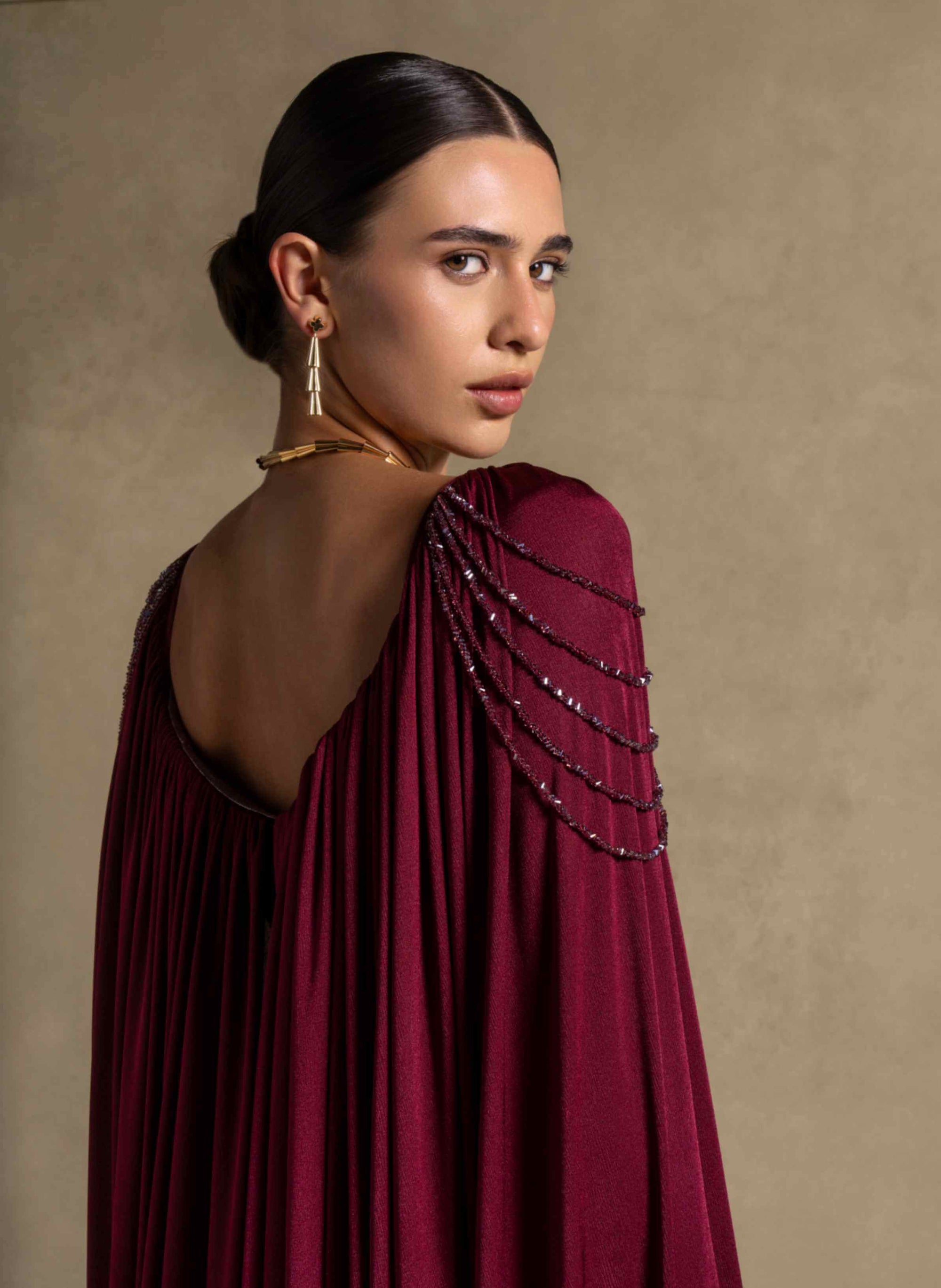Vionna Dress features a deep Maroon color, beaded shoulder accents, and draped jersey panels for luxury evening wear.